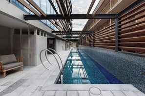 A modern indoor swimming pool with a clear glass ceiling, a lounge area with a sofa, and a view of the sky. - Lakeside Five star Comfort w Uninterrupted Views (Melbourne)