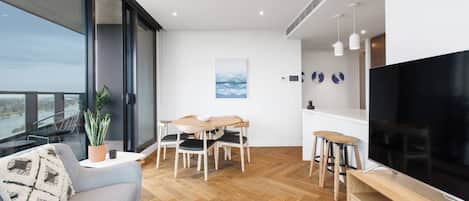 A modern living room with a large TV, wooden flooring, and a balcony with a view.