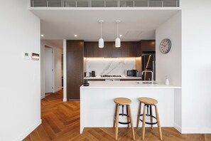 A modern kitchen with a white island, wooden stools, and a clock on the wall. - Lakeside Five star Comfort w Uninterrupted Views (Melbourne)