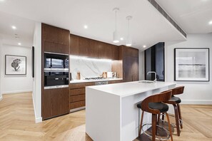 A modern kitchen with a central island, wooden cabinets, and a large window. - Top of Town Penthouse with Every Opulence (Melbourne)