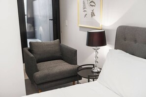A hotel room with a grey armchair, a bedside table with a lamp, and a bed with white bedding. - Top of Town Penthouse with Every Opulence (Melbourne)