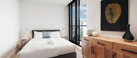 A modern bedroom with a large bed, a wooden dresser, a city view, and a leopard print artwork.