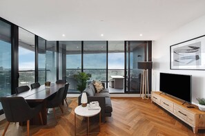 A modern living room with a dining area, large windows, a flat-screen TV, and a view of the city. - Top of Town Penthouse with Every Opulence (Melbourne)