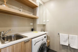 A modern kitchen with a stainless steel sink, a built-in washing machine, wooden shelves, and a towel rack. - BOWIE Sun soaked Comfort in the Heart of Richmond (Richmond)