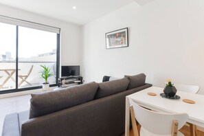 A modern living room with a grey sofa, a white dining table, and a TV on a black stand. - BOWIE Sun soaked Comfort in the Heart of Richmond (Richmond)