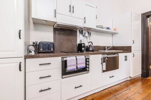 A modern kitchen with white cabinets, a granite countertop, a built-in oven, a coffee maker, and a toaster. - Elwood Manor A Restored Art Deco Gem (Elwood)