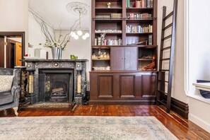 A living room with a fireplace, a bookshelf, and a ladder against the wall. - Elwood Manor A Restored Art Deco Gem (Elwood)