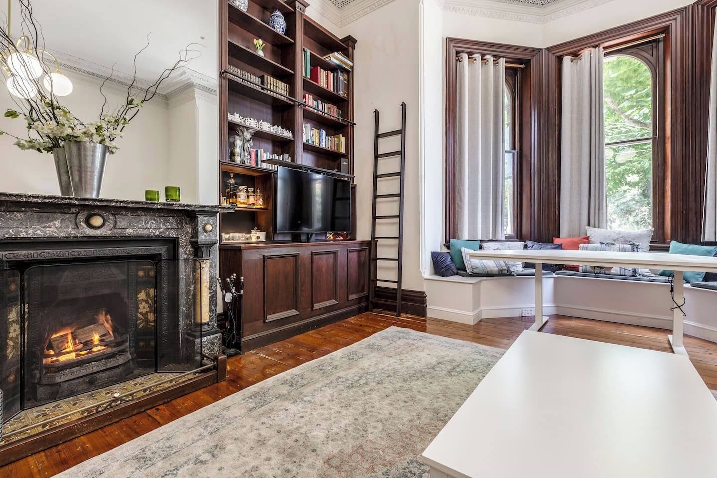 A living room with a fireplace, bookshelves, a television, and a window seat.