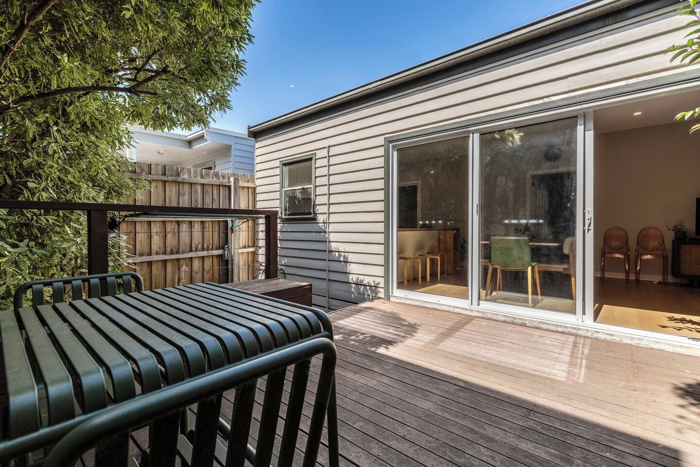 A modern house with a wooden deck, a sliding glass door leading to a dining area, and a visible outdoor seating arrangement.