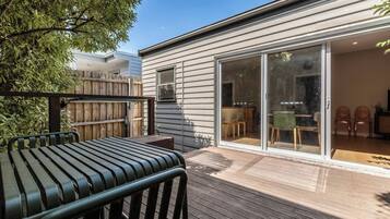 A modern house with a wooden deck, a sliding glass door leading to a dining area, and a visible outdoor seating arrangement.