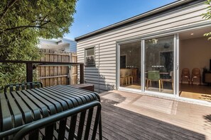 A modern house with a wooden deck, a sliding glass door leading to a dining area, and a visible outdoor seating arrangement. - Classic Comforts Moments to Flemington Racecourse (Flemington)