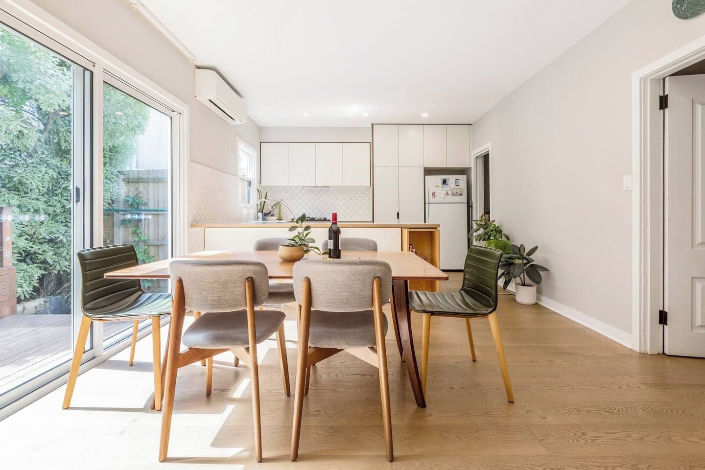 A modern kitchen with white cabinets, a dining table with four chairs, and a potted plant.