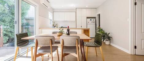 A modern kitchen with white cabinets, a dining table with four chairs, and a potted plant.