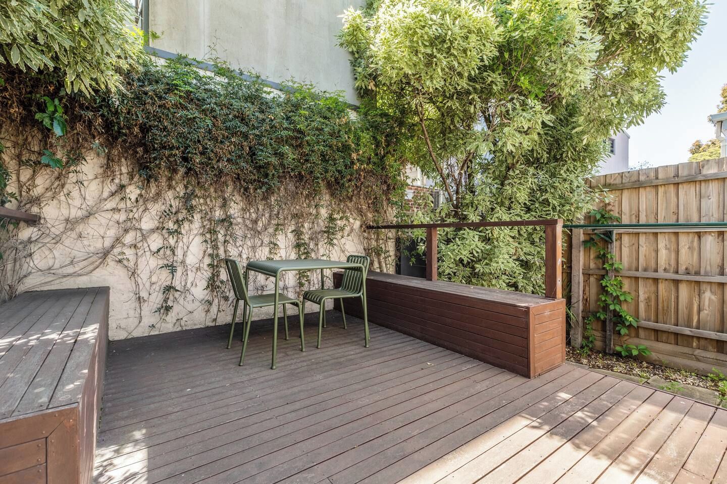 An outdoor patio with a wooden deck, a metal table with chairs, and a wooden bench.