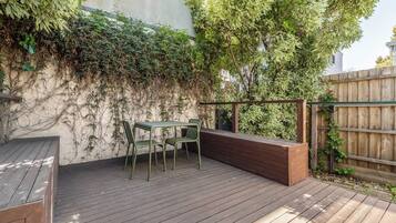 An outdoor patio with a wooden deck, a metal table with chairs, and a wooden bench.
