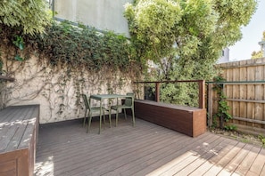 An outdoor patio with a wooden deck, a metal table with chairs, and a wooden bench. - Classic Comforts Moments to Flemington Racecourse (Flemington)
