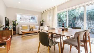 A modern living room with a dining area, large windows, and a view of greenery.