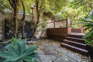 Ein Garten mit einer Holztreppe, die zu einer Terrasse führt, umgeben von Bäumen und Pflanzen.