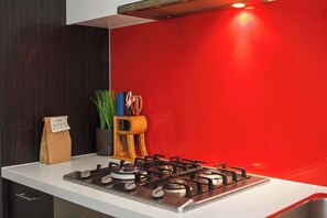A kitchen with a gas stove, a red backsplash, and a white countertop. - Dazzling Views from Contemporary High Rise Living (Melbourne)