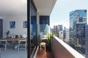 A balcony with a wooden table and chairs, a small round table with a plant, and a cityscape view. - Dazzling Views from Contemporary High Rise Living (Melbourne)