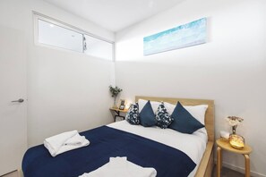 A bedroom with a bed, pillows, a bedside table with a lamp, a small plant, and a picture on the wall. - Dazzling Views from Contemporary High Rise Living (Melbourne)