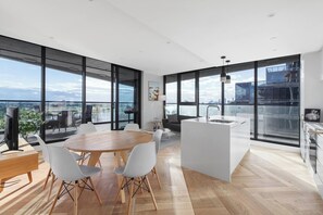 A modern kitchen with a central island, large windows, and a dining area with a round table and chairs. - Lakeside Lookout Modern Living with Majestic Views (Melbourne)