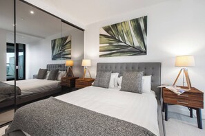 A modern hotel room with a large bed, two bedside tables with lamps, a large mirror, and artwork on the walls. - Lakeside Lookout Modern Living with Majestic Views (Melbourne)