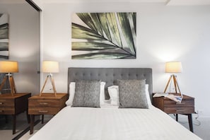 A hotel room with a large bed, two bedside tables, lamps, a grey upholstered headboard, and a large leaf-patterned artwork on the wall. - Lakeside Lookout Modern Living with Majestic Views (Melbourne)