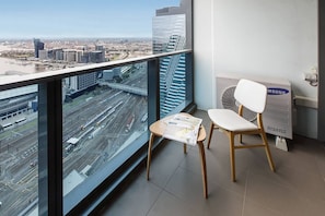A room with a view of a cityscape, a table with a magazine, a white chair, and a Samsung inverter on the floor. - Skyline Panorama in Melbourne CBD with Parking (Melbourne)