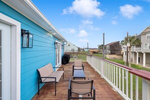 A wooden deck with outdoor seating, a covered barbecue grill, and a view of neighboring houses. - Stylish Galveston Island Getaway Near the Beach (Galveston)