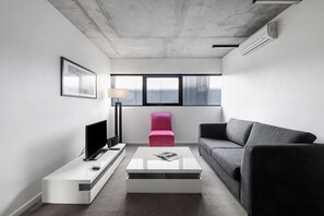 A modern living room with a flat-screen TV, a coffee table, a sofa, and a pink chair. - Refresh at Rhapsody City Fringe Contemporary (Melbourne)
