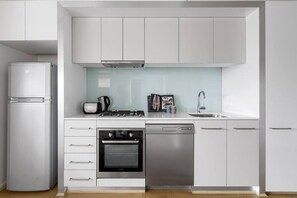 A modern kitchen with white cabinetry, a built-in oven, a dishwasher, a gas stove, and a refrigerator. - Refresh at Rhapsody City Fringe Contemporary (Melbourne)