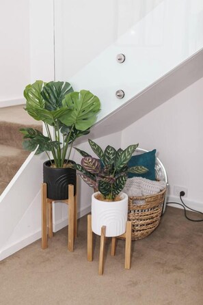 A staircase with a white railing, two potted plants on wooden stands, and a wicker basket with a cushion. - Metropolis Icon Bourke Street Heritage Hideaway (Melbourne)