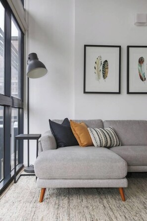A modern living room with a grey sofa, a small side table, and a floor lamp. There are two framed artworks on the wall. - Metropolis Icon Bourke Street Heritage Hideaway (Melbourne)