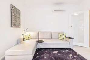 A modern living room with a sofa, a remote control on a side table, a patterned rug, and a wall-mounted air conditioner. - The Courtyard Chateau Fresh and Modern off Toorak Rd (South Yarra)