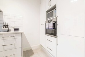 A modern kitchen with white cabinetry, a microwave, an oven, and a digital scale on the counter. - The Courtyard Chateau Fresh and Modern off Toorak Rd (South Yarra)