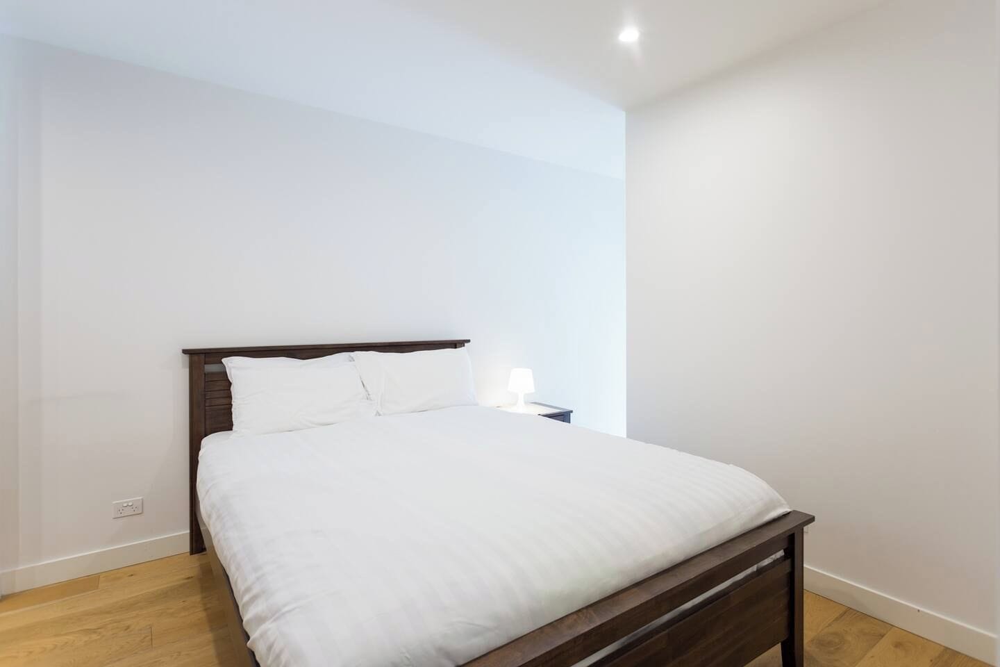 A single bed with a wooden headboard in a room with white walls and a wooden floor.