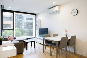 A modern living room with a sofa, TV, dining table, chairs, and a large window. - Urban Stay in Trendy Windsor close to Chapel St (Windsor)
