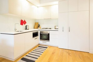 A modern kitchen with white cabinetry, a stainless steel sink, a kettle, and a stove. - Urban Stay in Trendy Windsor close to Chapel St (Windsor)