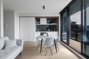 A modern apartment with a dining area, kitchen, and a large window offering a city view. - South Yarra Serenity on Chapel St with City Views (South Yarra)