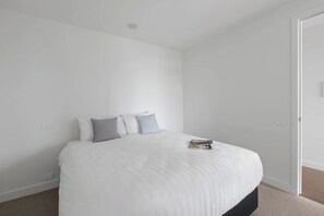 A minimalist bedroom with a large bed, a single nightstand, and a door to the right. - South Yarra Serenity on Chapel St with City Views (South Yarra)