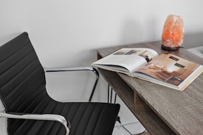 A black office chair with a metallic frame, a wooden table, and a magazine with images of furniture. - South Yarra Serenity on Chapel St with City Views (South Yarra)