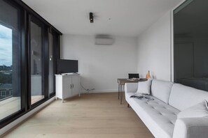 A modern living room with a sofa, a TV on a cabinet, and a small table with a lamp. - South Yarra Serenity on Chapel St with City Views (South Yarra)