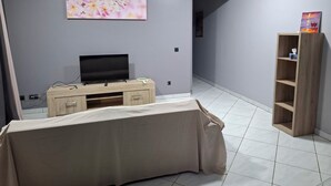 A room with a television on a wooden stand, a painting on the wall, and a wooden shelf with a book. - KEYKI HOME (PIRAE)