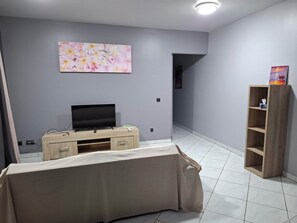 A room with a television on a wooden stand, a painting on the wall, and a wooden shelf with a book. - KEYKI HOME (PIRAE)