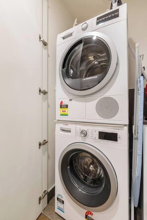A stacked washer and dryer unit with control panels and a door. - Parque Canopy Lakeside Living with Infinity Pool (Melbourne)