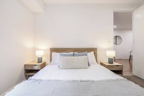 Une chambre à coucher avec un grand lit, deux tables de chevet avec des lampes, une tête de lit en bois et un miroir au mur.
