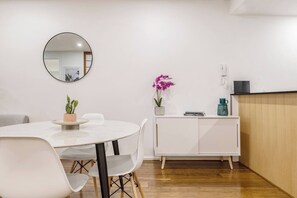 Un espace repas moderne avec une table ronde, des chaises blanches, une petite plante en pot, un meuble blanc et un miroir au mur.