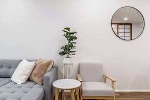 Une pièce avec un canapé gris, une table ronde, une chaise, une plante en pot et un miroir au mur.
