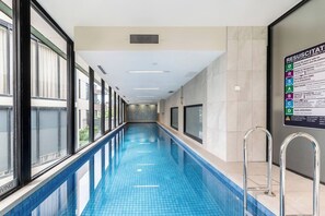 Une longue piscine intérieure aux parois en verre transparent, dotée d’un sol carrelé et affichant sur un mur un poster contenant des instructions de sécurité en cas d’urgence.